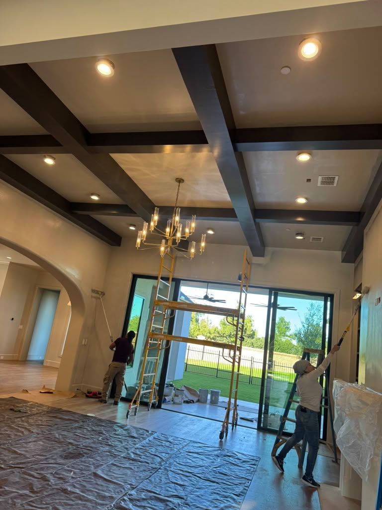 Modern living room under renovation with exposed beams, chandelier, and workers near a glass doorway
