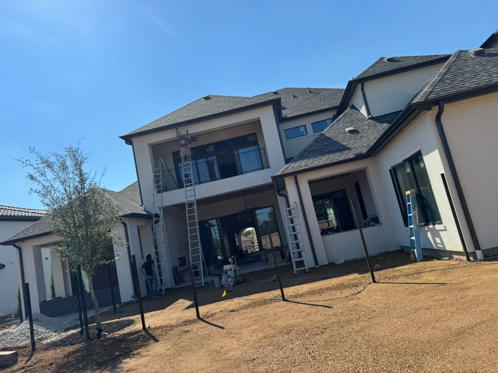 Modern two-story house with stucco exterior, dark roof, and dry front yard under a clear blue sky