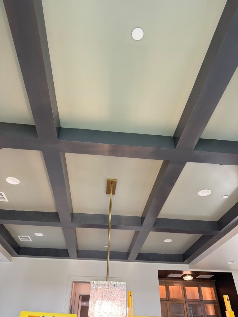 Decorative coffered ceiling with dark beams, recessed lights, and a hanging pendant in a bright room