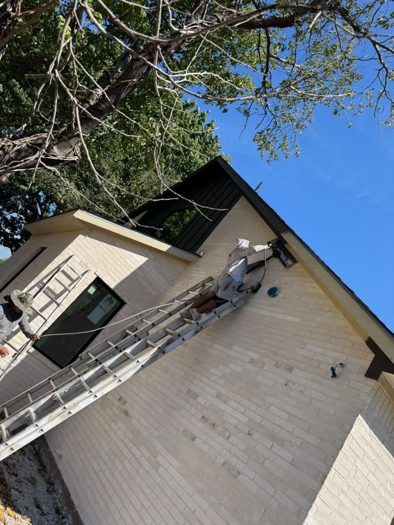 Ladder leaning against a house roof with workers near the eaves under a blue sky