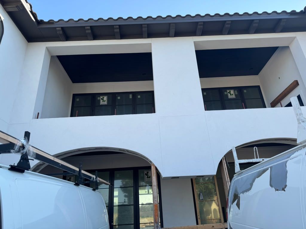 White modern building facade with arched entrances and balcony, viewed from below.