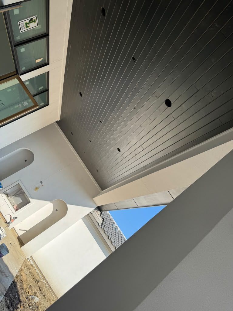 Modern courtyard with black slatted ceiling, white walls, and skylights above stone details