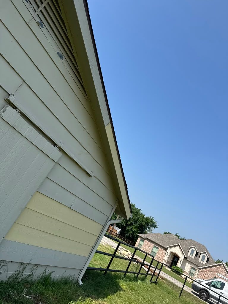 Side of a white house with green lawn, wooden fence, and neighboring houses under a blue sky.