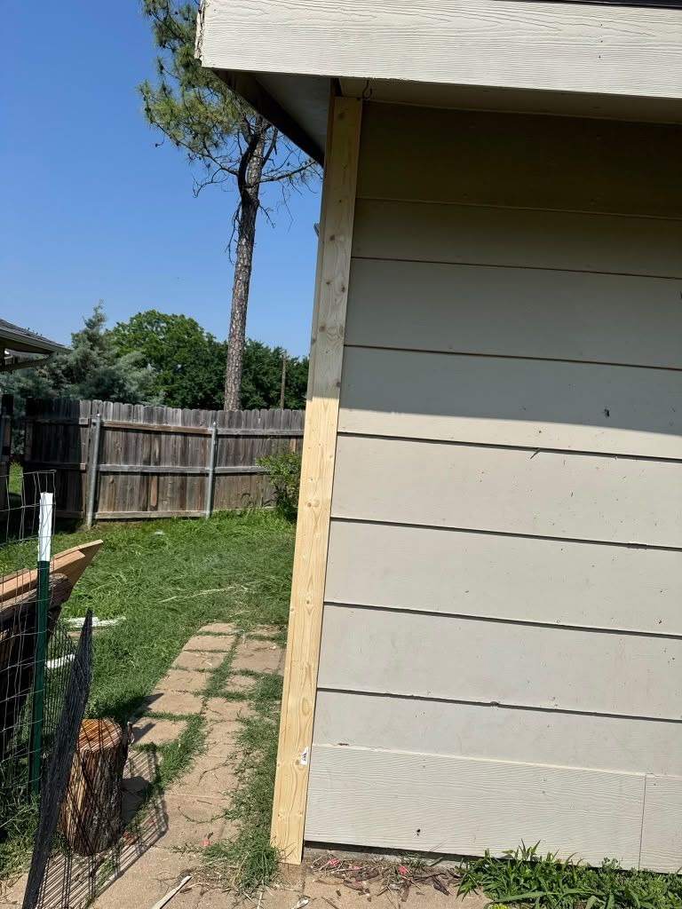Side of a beige house beside a grassy yard, wooden fence, and blue sky.