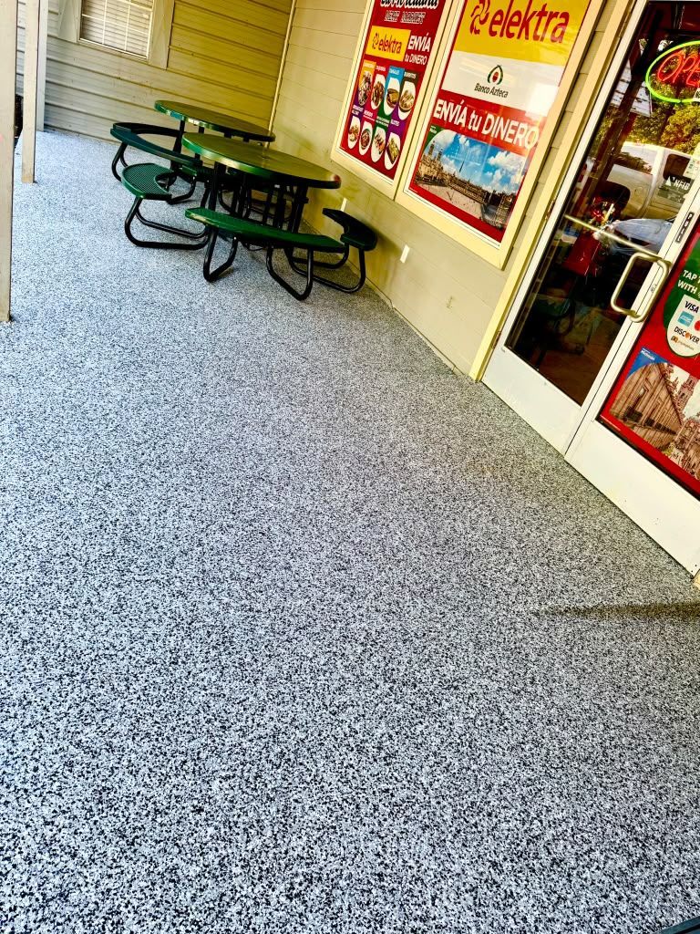 Storefront walkway with green picnic tables and red-framed windows on a speckled floor