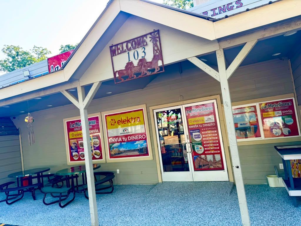 Convenience store storefront with colorful window signs, picnic tables, and a covered entryway