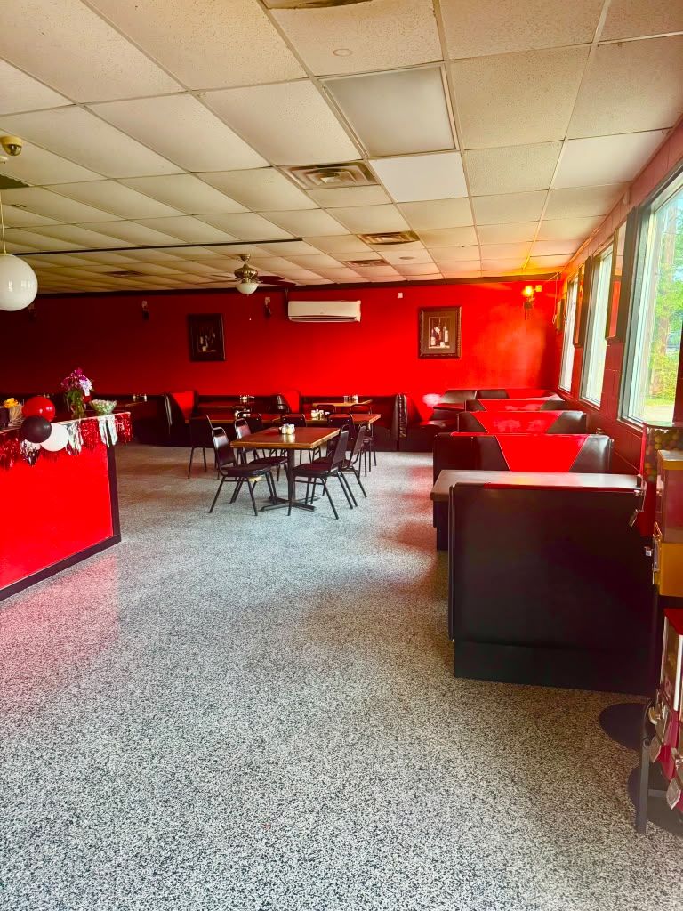 Red lounge with red walls, black seating, tables, and large windows along the right side.