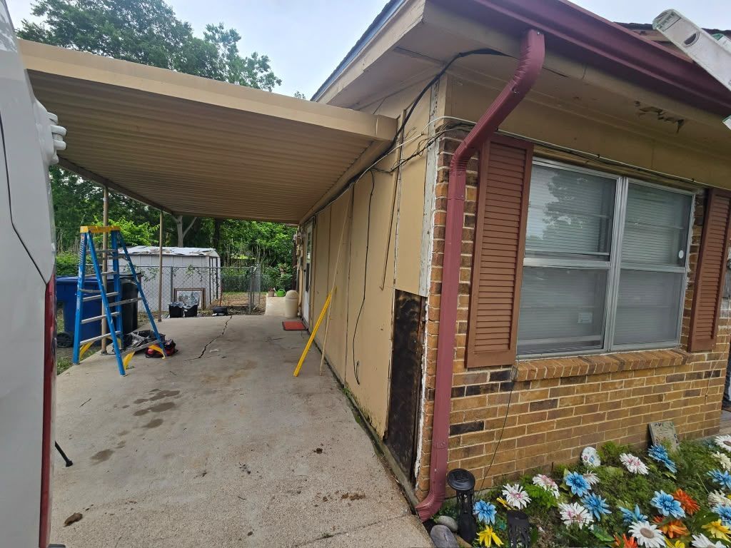 Carport beside a brick house with a window, driveway, and colorful flowers along the foundation.