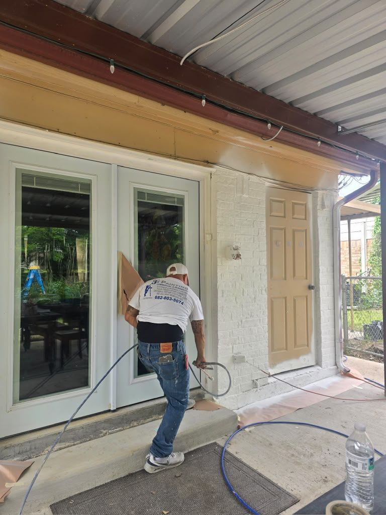 Worker painting exterior wall beside sliding glass door and beige entry door under covered porch