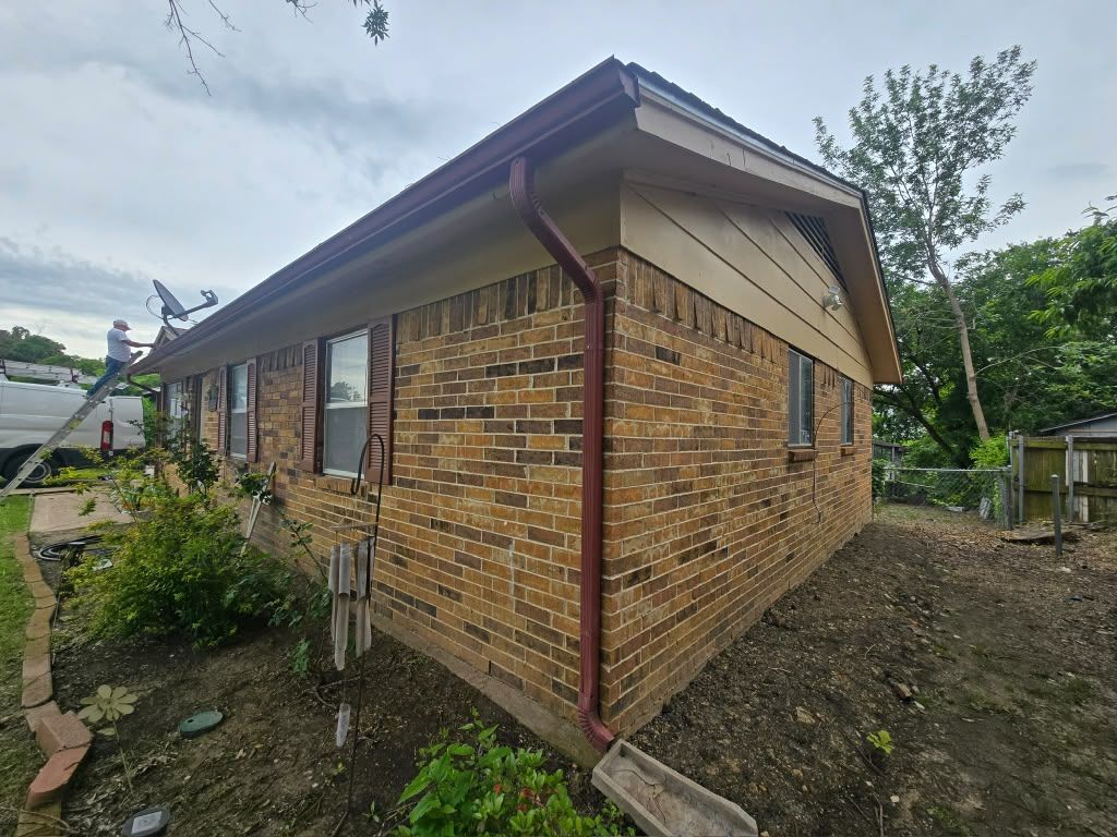 Single-story brick house exterior with brown roof and gravel yard, viewed from the side