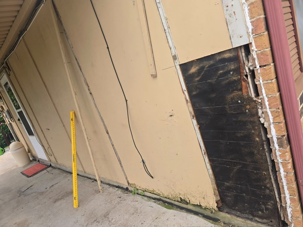 Tilted view of a beige building wall with a black boarded-up doorway and a yellow pole leaning nearby.