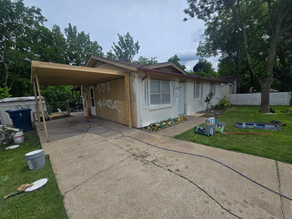 Partially demolished house with a carport, broken windows, and debris on a driveway and lawn