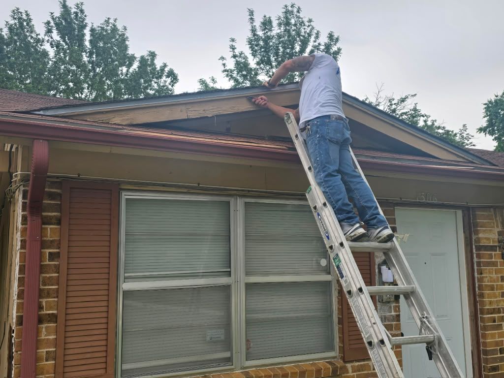 Person on a ladder repairing the roof of a brick house.