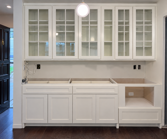 White built-in cabinets and glass-front upper cupboards in a bright kitchen or laundry room.