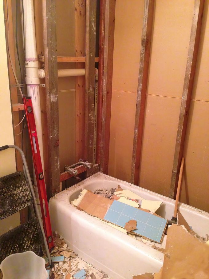 Bathroom under renovation with exposed wall studs and a white tub filled with construction debris.