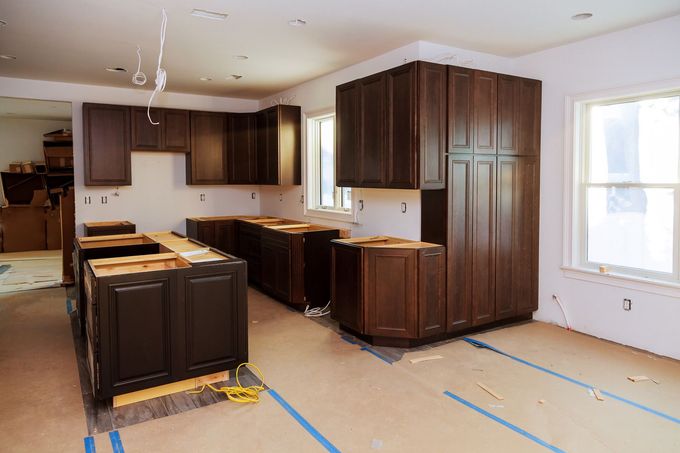 Unfinished kitchen with dark wood cabinets, island, and taped floor near bright windows.