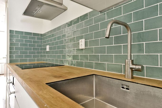 Modern kitchen with green tile backsplash, wooden counter, stainless sink, and range hood