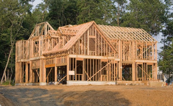 Wooden house frame under construction on a cleared lot, with roof trusses and exposed framing.