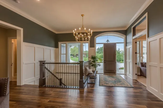 Elegant foyer with dark wood floors, chandelier, staircase, and open front door to daylight