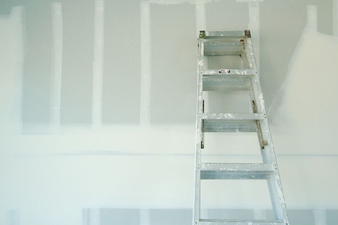 Silver ladder leaning against a white drywall wall under construction