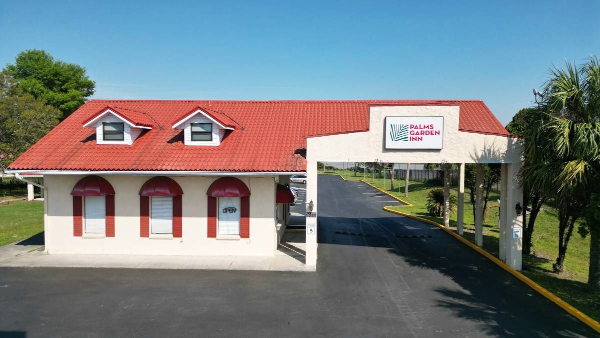 Small white building with red roof and awnings beside a covered driveway entrance on a sunny day