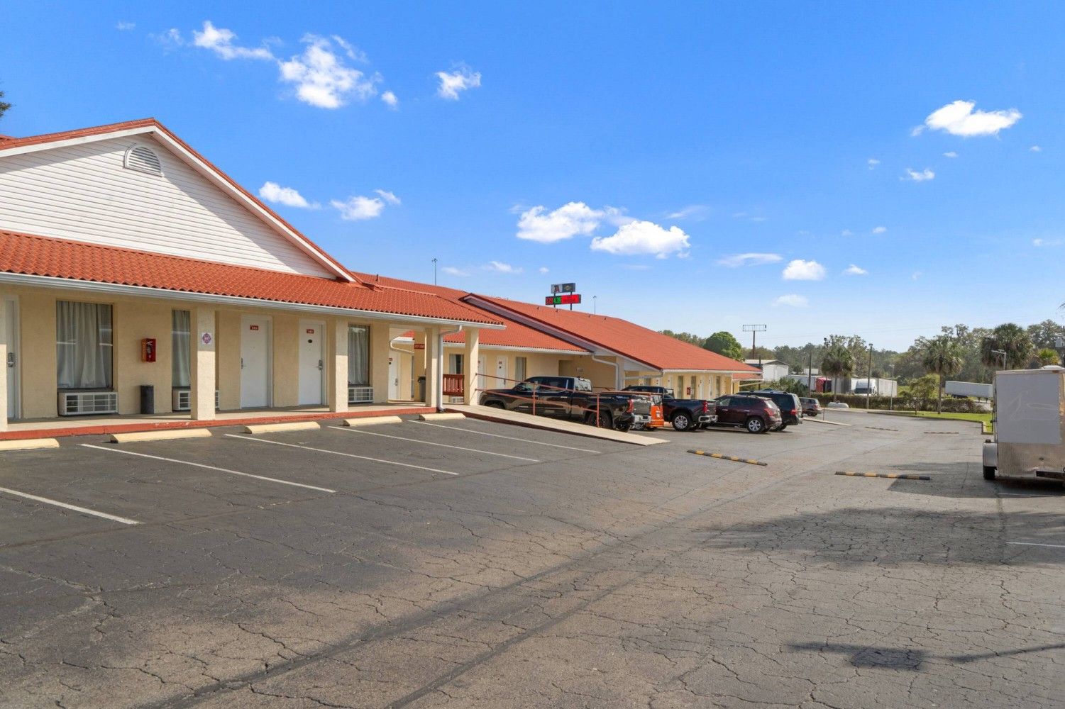 Strip-mall storefronts with red tile roofs beside a nearly empty parking lot under a blue sky