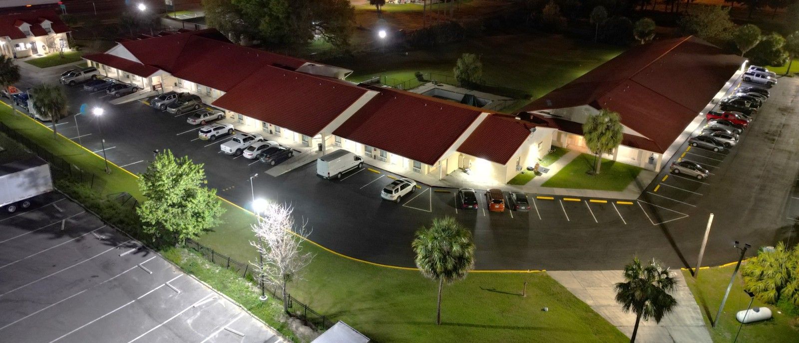 Aerial night view of a brightly lit shopping center with red roofs and an empty parking lot