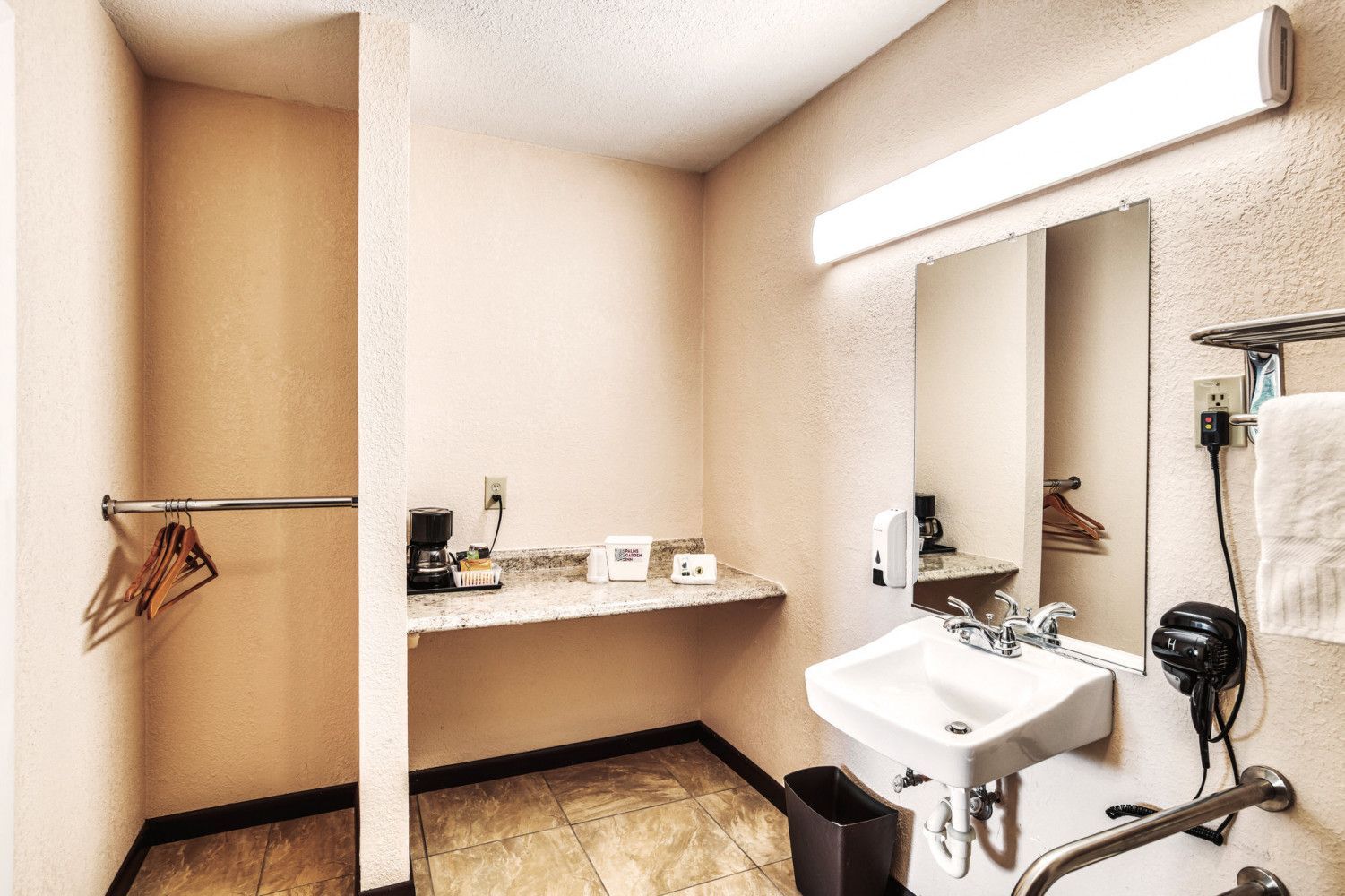 Small restroom with a sink, mirror, hair dryer, and changing area with hanging clothes
