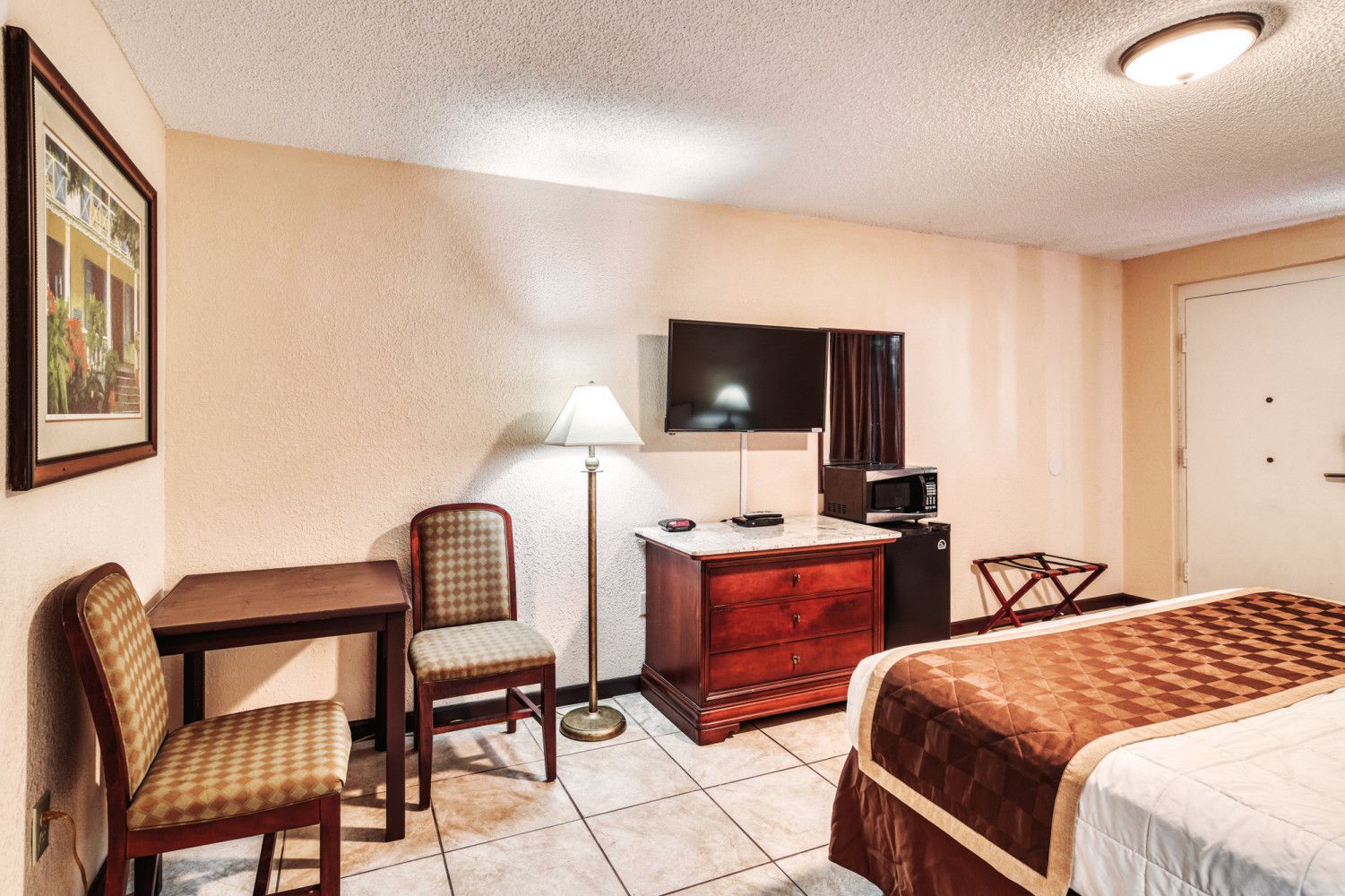 Hotel room with a bed, TV, dresser, chair, and tiled floor