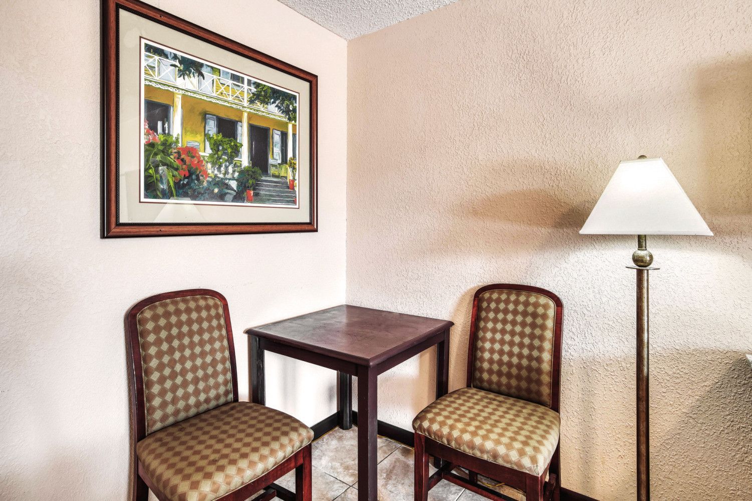 Small seating nook with two chairs, a table, framed art, and a floor lamp against beige walls.