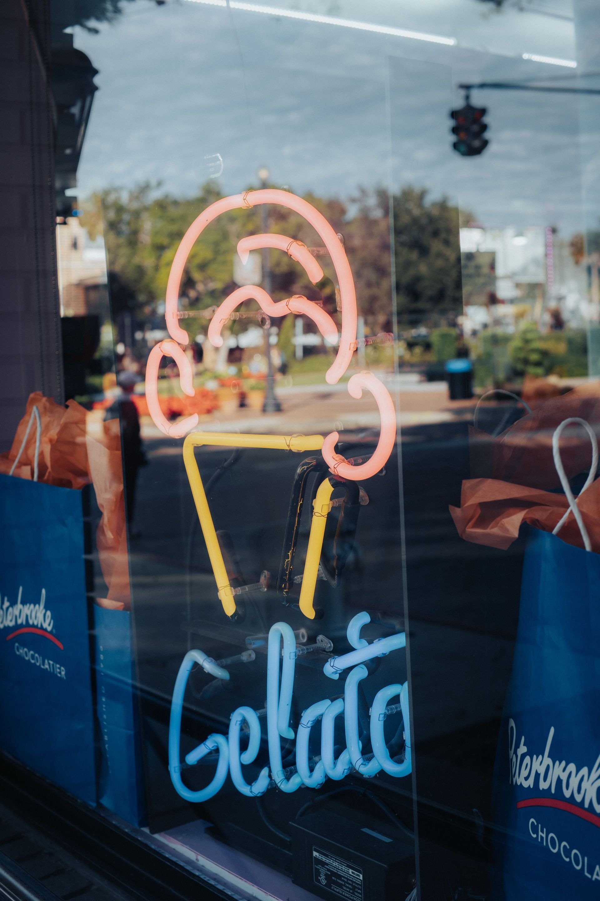 Neon gelato cone sign on a storefront window with reflections outside
