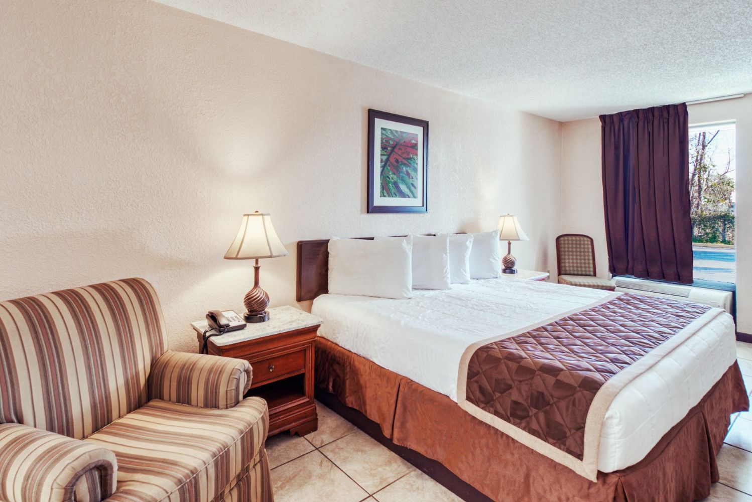 Hotel room with two beds, striped armchair, nightstand lamps, and a window with purple curtains