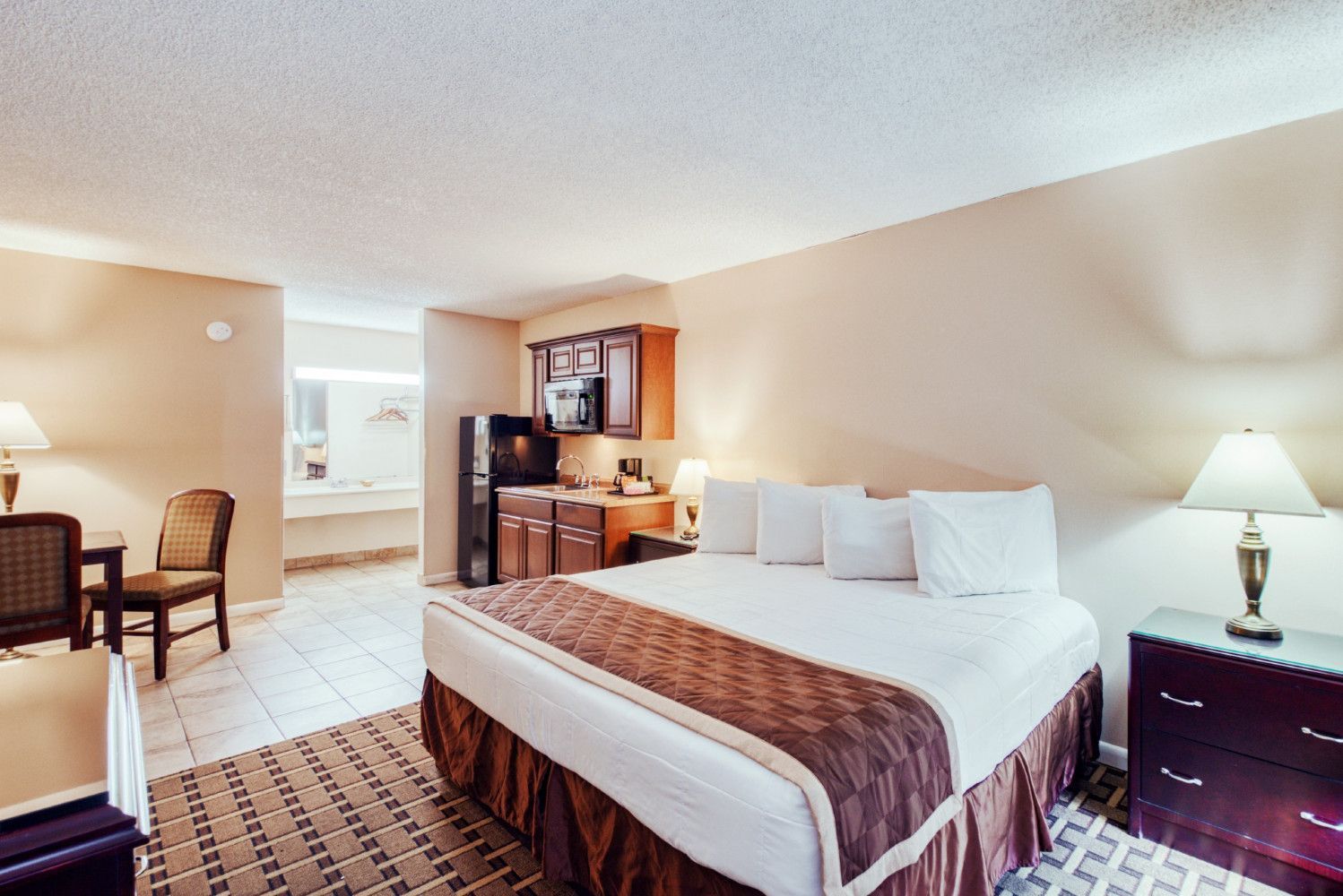 Hotel room with a king bed, desk, dresser, and warm beige decor