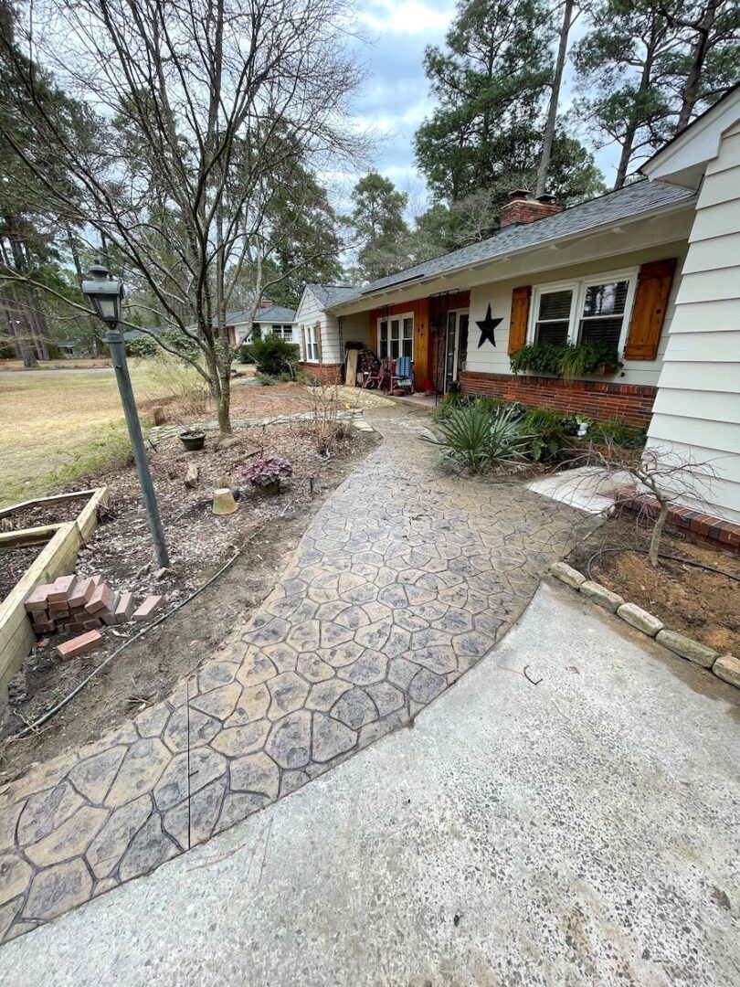 A stamped concrete walkway leads to the front porch of a light-sided house with a visible star decoration on the wall.