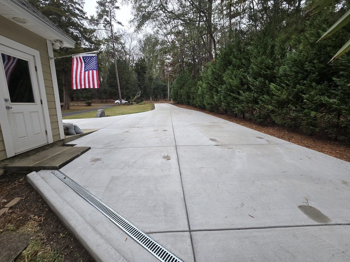 A concrete driveway leads toward trees beside a building with an American flag hung by the door.