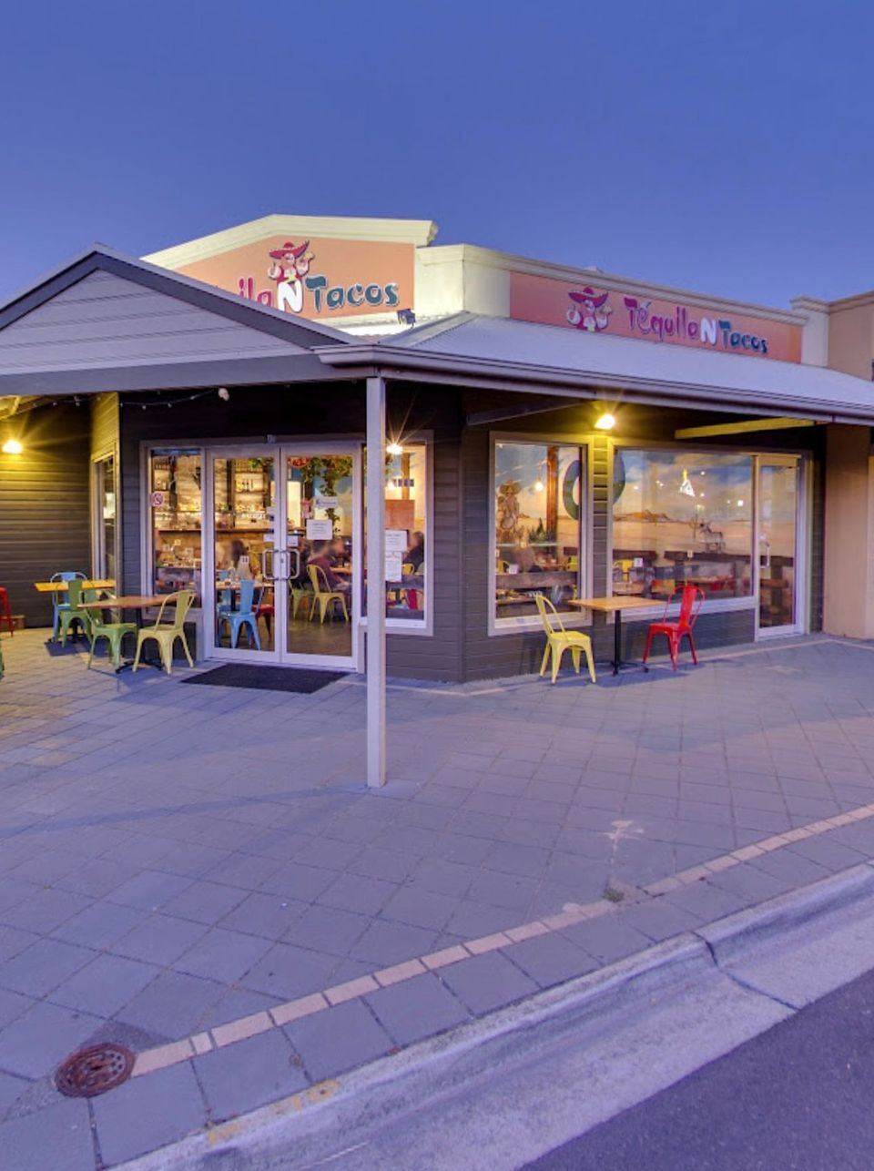 Exterior of a Fuzzy's Taco Shop restaurant with colorful chairs and windows.