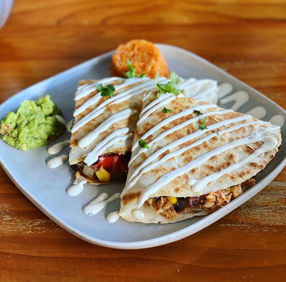 Quesadillas with toppings, guacamole, and a side of mashed sweet potato on a plate.