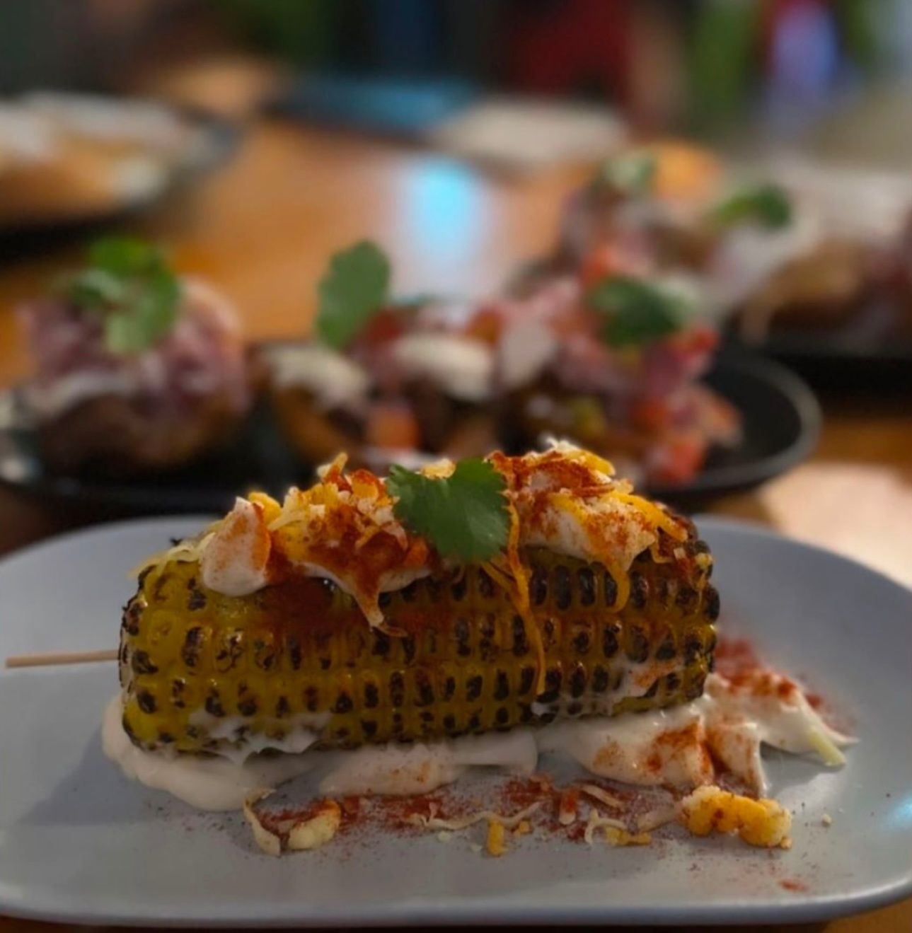 Grilled corn on a plate, topped with sauce and cheese