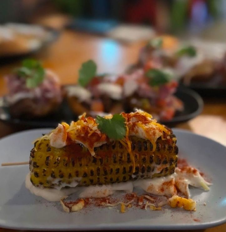 Grilled corn on a plate, topped with sauce and cheese