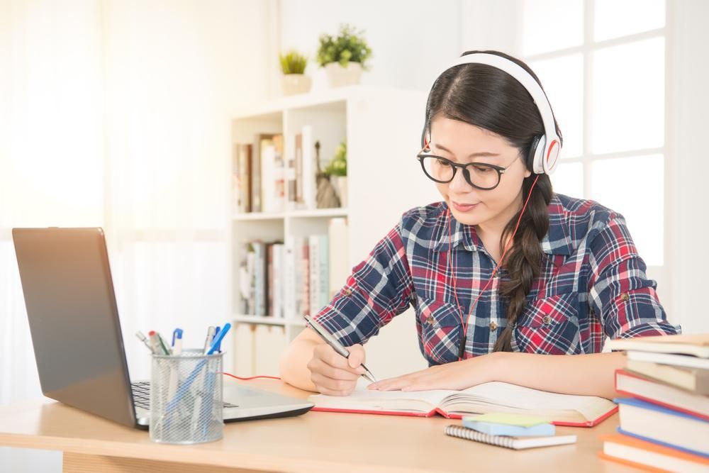 A Girl Wearing Headphones Is Sitting at A Desk with A Laptop and Books — Al Roberts Education Centre in Wynnum West, QLD