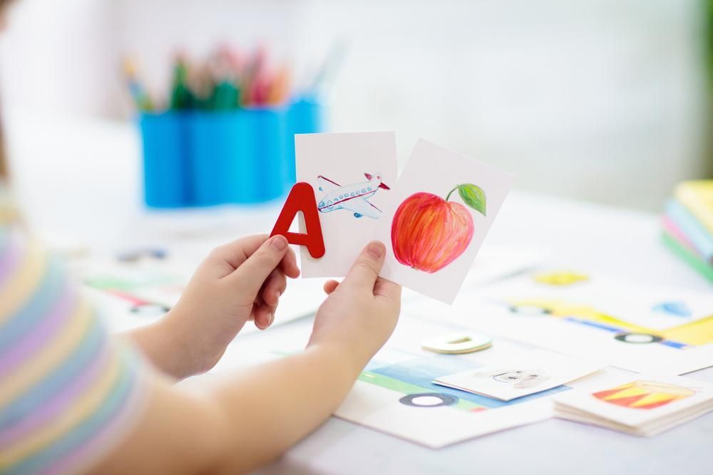 A child is holding a cards with the letter a and an apple on them — Al Roberts Education Centre in Wynnum West, QLD