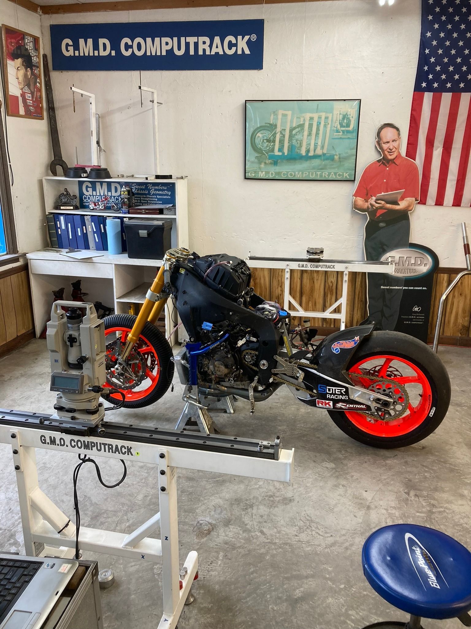 A motorcycle is sitting on a stand in a room with a sign that says g.m.d. computrack