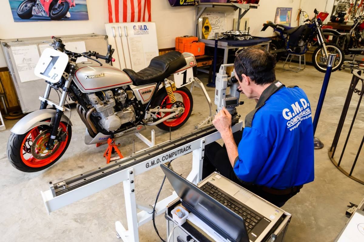 A man wearing a blue shirt that says gala is working on a motorcycle