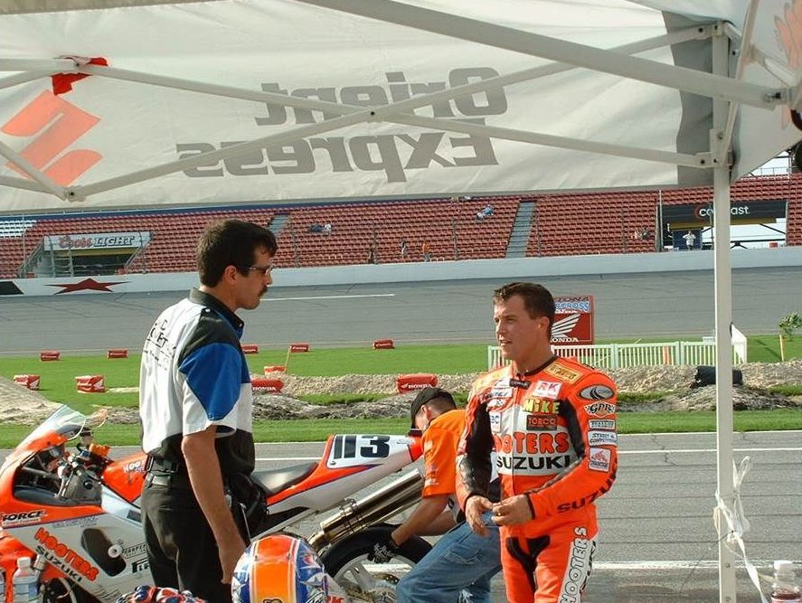 A man in a suzuki shirt is talking to another man