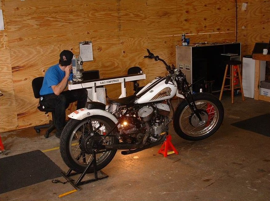 A man sits at a desk next to a white motorcycle