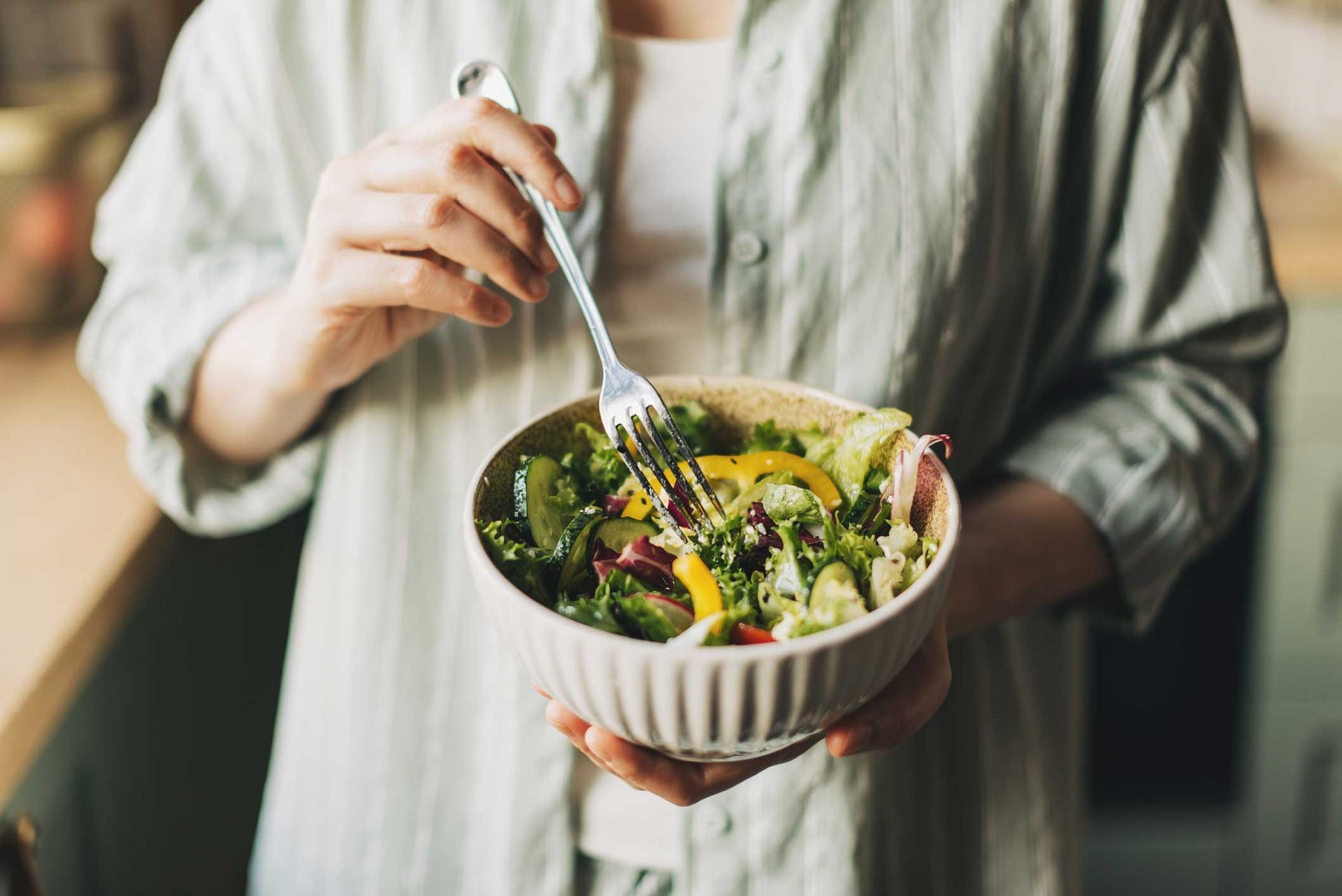 Person holding a bowl of salad, preparing to eat; green shirt, kitchen setting. Person holding a bowl of salad, preparing to eat; green shirt, kitchen setting.
