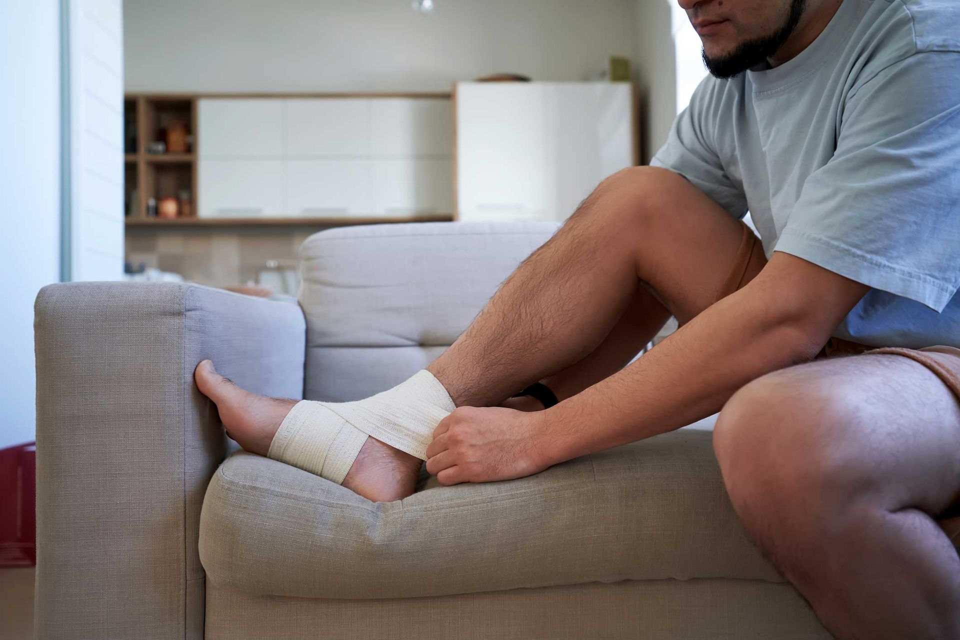 Man wrapping ankle with bandage on a couch. Man wrapping ankle with bandage on a couch.