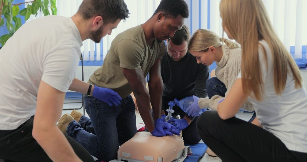 Group of people practicing CPR on a dummy; indoors with sunlight.