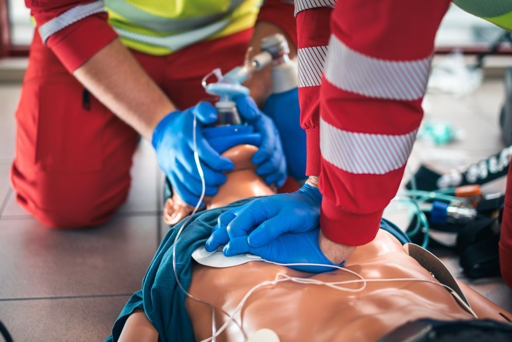 Paramedics performing CPR on a mannequin, one administering oxygen with a mask.