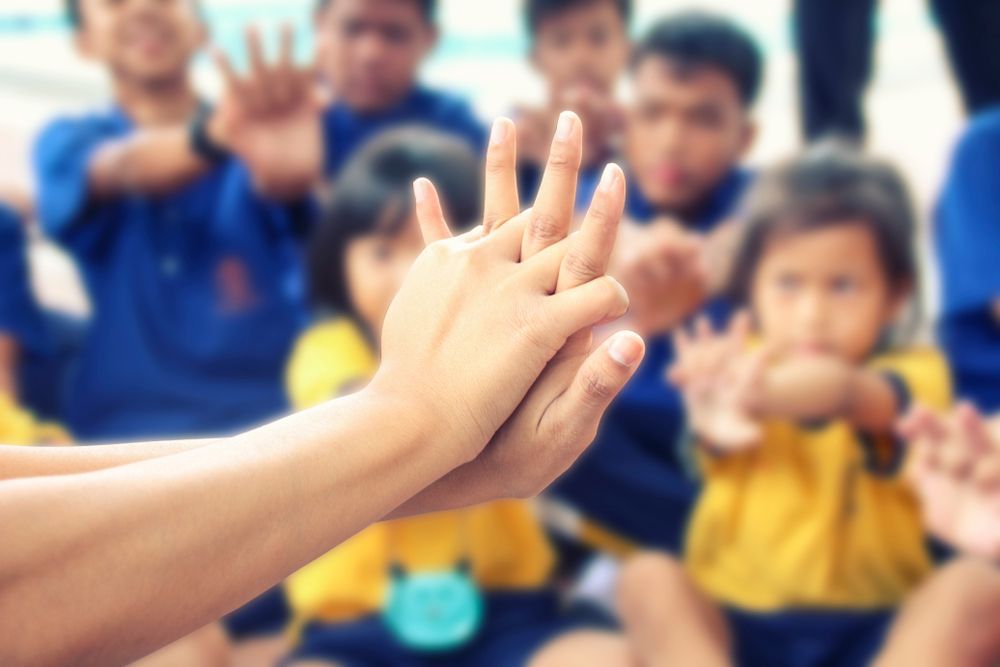Hands demonstrating CPR on a person, children watching in the background.